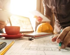 Hands of two workers at desk with hard hat in background