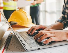 hands typing on laptop with hard hat in background