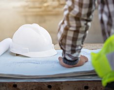 Worker in green vest working on paper plans with white hardhat in background