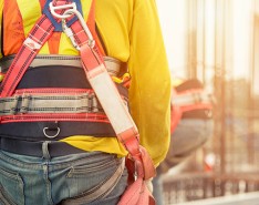 A construction worker is walking away from the camera, wearing a safety harness