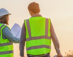 Man and woman in construction vests and hardhat looking at papers on jobsite