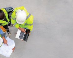 Three people in hard hats and vests talking and looking at files