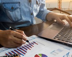 Person seated at desk, using a laptop and looking at charts