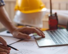Hands in front of laptop with hard hat in background