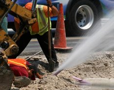 Water spews out of ground while two workers inspect nearby