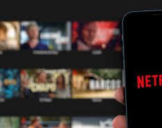 Smart phone with Netflix logo in front of larger screen showing Netflix library