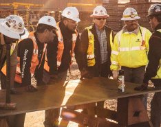 Six men in construction uniforms stand around a table