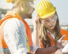 A male construction worker and a female construction worker look at blueprints