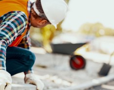 A person in a hard hat and bright orange safety vest looks at a road construction site