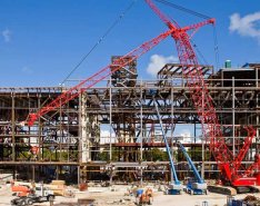 A large red crane sits in front of a building under consruction