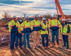 Eight people in bright safety jackets stand on a construction site