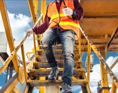 A person wearing jeans and a bright safety vest descends metal stairs holding the railing with one hand