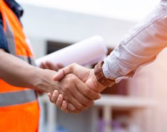 A person in a bright safety vest, holding paper in one hand, shakes hands with someone in a long sleeve shirt.