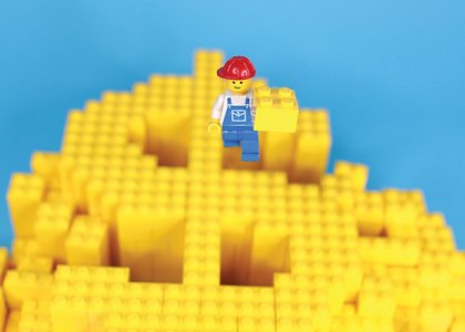 Lego blocks in the shape of a dollar bill with a Lego construction worker on top / Adobe Stock 