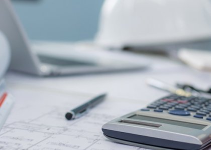 calculator on top of blueprints with hard hat in the background 