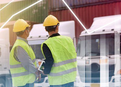 Two construction workers in hard hats and vests look at vehicle fleet / Adobe Stock 