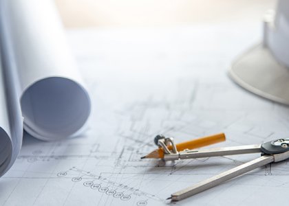 Pencil and compass on top of blueprints, with hard hat off to the side