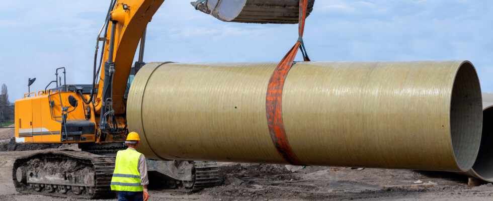 excavator hoisting a concrete pipe