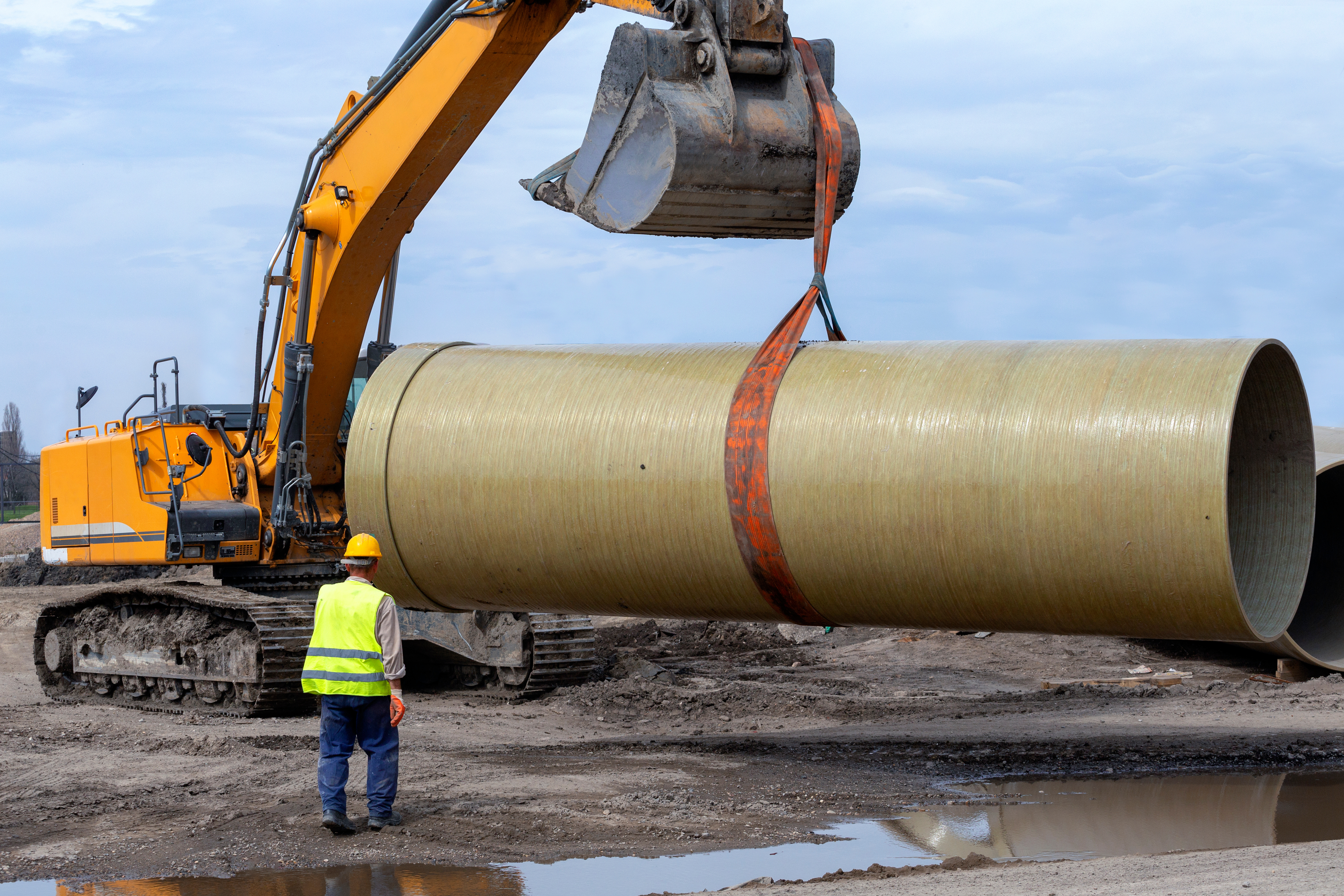 excavator hoisting a concrete pipe