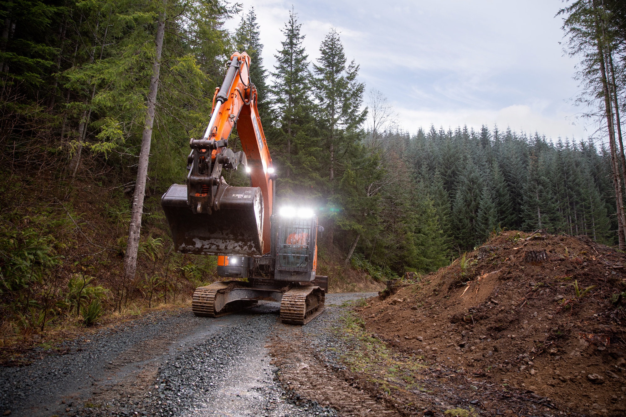 Develon machine driving on forest road with lights shining