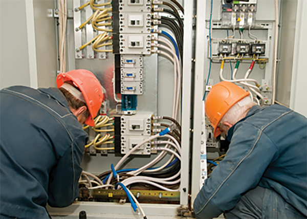 Two electricians working inside electrical panel