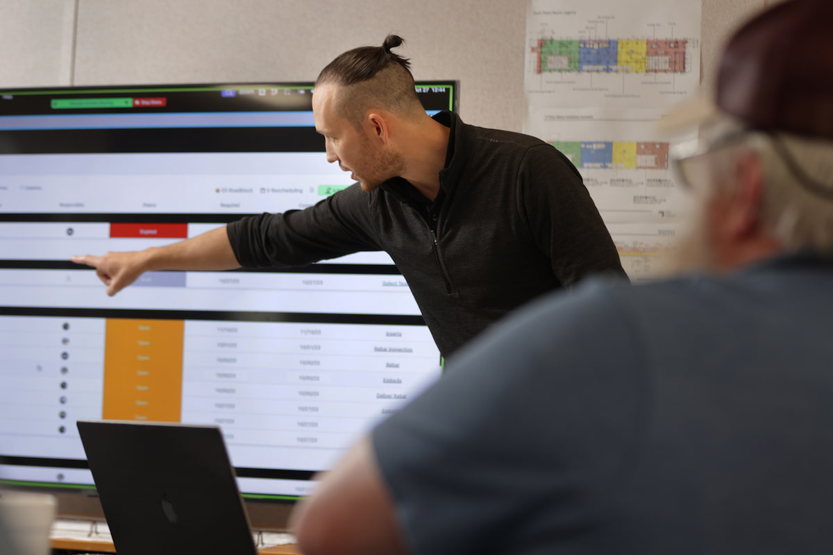 Construction team reviewing a digital project schedule on computer screens in an office setting.