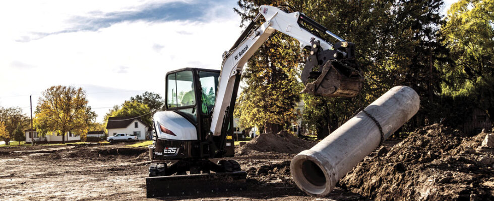 Excavator lifting concrete pipe at construction site