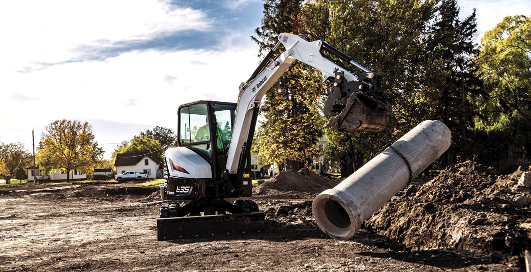 Excavator lifting concrete pipe at construction site